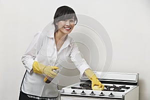 Portrait of young housemaid cleaning stove against gray background