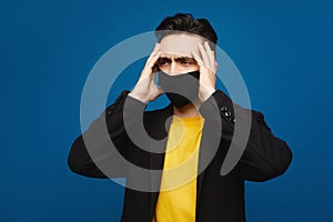 Portrait of young ill man in medical protective mask on face suffering from headache and weakness, isolated at blue