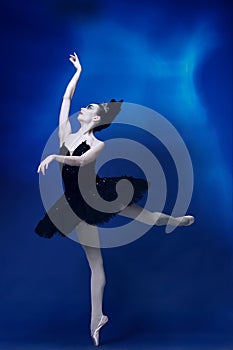 Portrait of young incredibly beautiful woman, ballerina in black ballet outfit, tutu dancing at blue studio full of