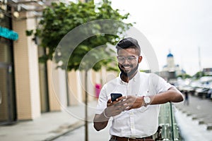 Portrait of young Indian businessman using mobile phone in the streets outdoors