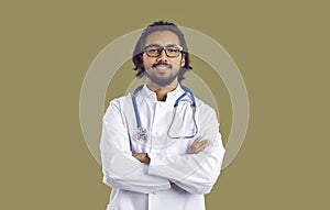 Portrait of young Indian doctor in white coat with stethoscope standing with his arms folded