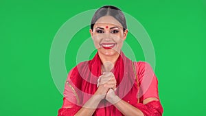 Portrait of a young Indian girl with red bindi dot in national classic red sari looking straight, smiles and folded palm