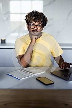 Portrait of a young indian man with a beard drinking some coffee and using laptop computer to work from home