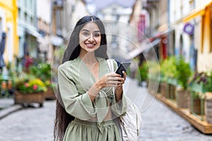 Portrait of a young Indian woman in a national green suit using a mobile phone while walking outside in the city