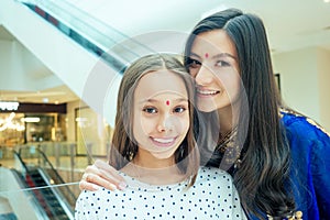 Portrait of a young indian woman wearing blue sari and gold bracelet having fun with her cute daughter in shopping mall