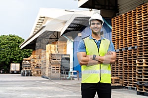 Portrait of young Indian worker with arm folded working in logistic industry in front of factory warehouse. Smiling