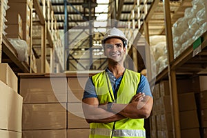Portrait of young Indian worker with arm folded working in logistic industry indoor inside factory warehouse. Smiling