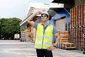 Portrait of young Indian worker working in logistic industry outdoor in front of factory warehouse. Smiling happy man