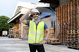 Portrait of young Indian worker working in logistic industry outdoor in front of factory warehouse. Smiling happy man