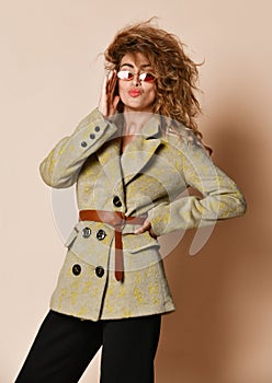 Portrait of young insolent woman with curly hair standing in designer grey winter jacket and fashion sunglasses
