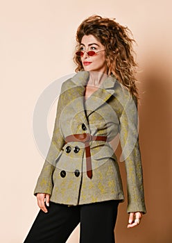 Portrait of young insolent woman with curly hair standing in designer grey winter jacket and fashion sunglasses