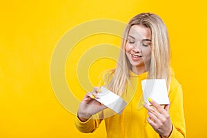 Portrait of young joyful caucasian blonde woman in yellow sportive suit, open a white gift box, isolated on yellow background