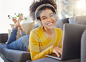 Portrait of a young joyful mixed race woman wearing headphones and listening to music while working on a laptop at home