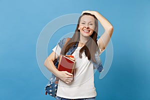 Portrait of young joyful smiling woman student with backpack touching correcting her hairstyle, holding school books