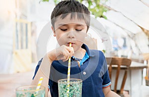 Portrait Young kid drinking fresh juice for breakfast in cafe,Happy child boy drinking glass of soda or soft cold drink while