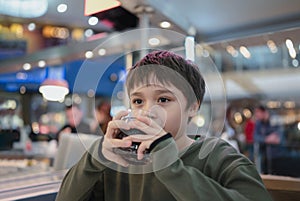 Portrait of  Young kid sitting on table drinking cold drink in restaurant, A boy drinking soda or soft drink from glass, Child boy