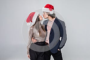 Portrait of young kissing couple in Christmas hats  over white background