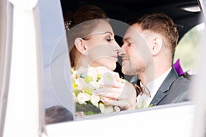 Portrait of a young kissing couple in love with a newlywed couple next to a bouquet in the window of a wedding car.