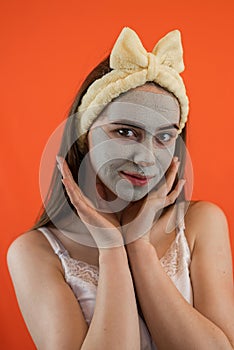 Portrait of young lady with green nourishing caly mask on face isolated on orange