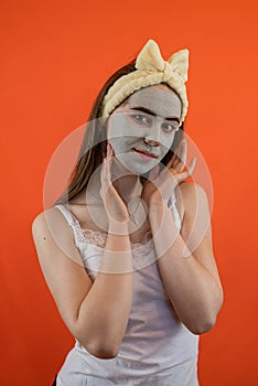 Portrait of young lady with green nourishing caly mask on face isolated on orange