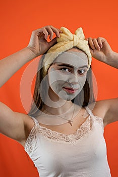 Portrait of young lady with green nourishing caly mask on face  on orange
