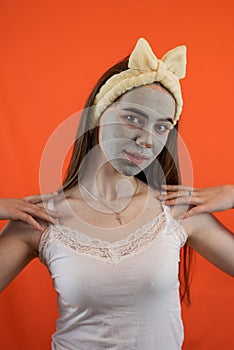 Portrait of young lady with green nourishing caly mask on face  on orange