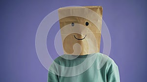 Portrait of young lady with paper bag on head moving to camera with smiling face