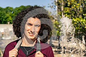 Portrait of a young latin man with curly hair smiling in a public park