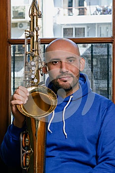 portrait of young latin man saxophonist sitting at home with his saxophone looking at the camera