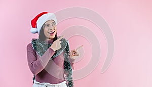 Portrait of young latin woman pointing finger to copy space in a christmas concept on pink background