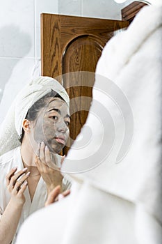 Portrait of a young Latina woman just out of the shower with a towel on her head putting on a facial mask cream