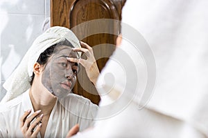 Portrait of a young Latina woman just out of the shower with a towel on her head putting on a facial mask cream