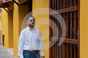 Portrait of a young Latino man dressed in white. He walks down the street of his neighborhood in the city