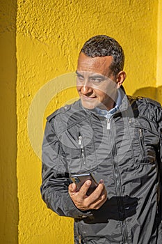 Portrait of a young Latino man leaning against a yellow wall