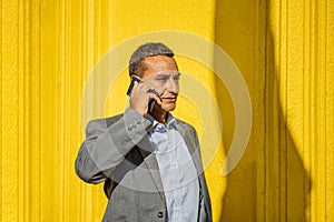 Portrait of a young latino man talking on the mobile phone isolated on yellow background