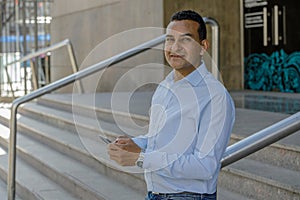 Portrait of a young Latino man using a mobile phone on the stairs of a building