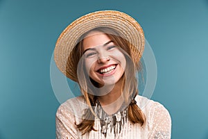 Portrait of a young laughing girl in summer hat isolated over blue background