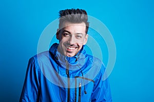 Portrait of a young laughing man in a studio with anorak on a blue background.