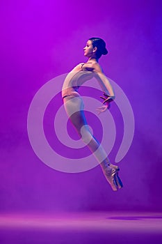 Portrait of young little ballet dancer, teen jumping  on purple background in neon light. Art, grace, beauty