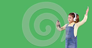 Portrait of young little school girl standing against green background holding the smart phone in her hand and listening