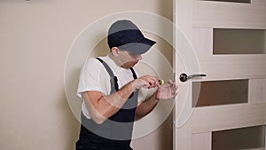 Portrait of young locksmith workman in blue uniform installing door knob.