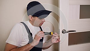 Portrait of young locksmith workman in blue uniform installing door knob.