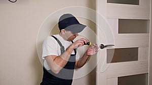 Portrait of young locksmith workman in blue uniform installing door knob.