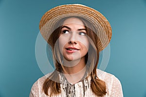 Portrait of a young lovely pensive girl in summer hat isolated over blue background,