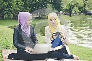 Portrait of young lovely pleasant mix ethnic woman sitting on grass at summer green park and having a discussion