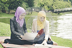 Portrait of young lovely pleasant mix ethnic woman sitting on grass at summer green park and having a discussion