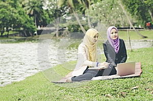 Portrait of young lovely pleasant mix ethnic woman sitting on grass at summer green park and having a discussion