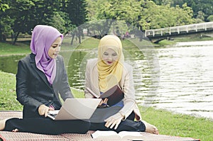 Portrait of young lovely pleasant mix ethnic woman sitting on grass at summer green park and having a discussion