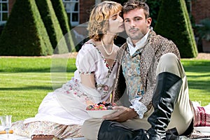 Portrait of young lovers dressed in vintage clothing. Handsome man looking at camera as his partner kisses him on cheek.