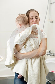 Portrait of young loving caring mother huggging her baby after washing in bath